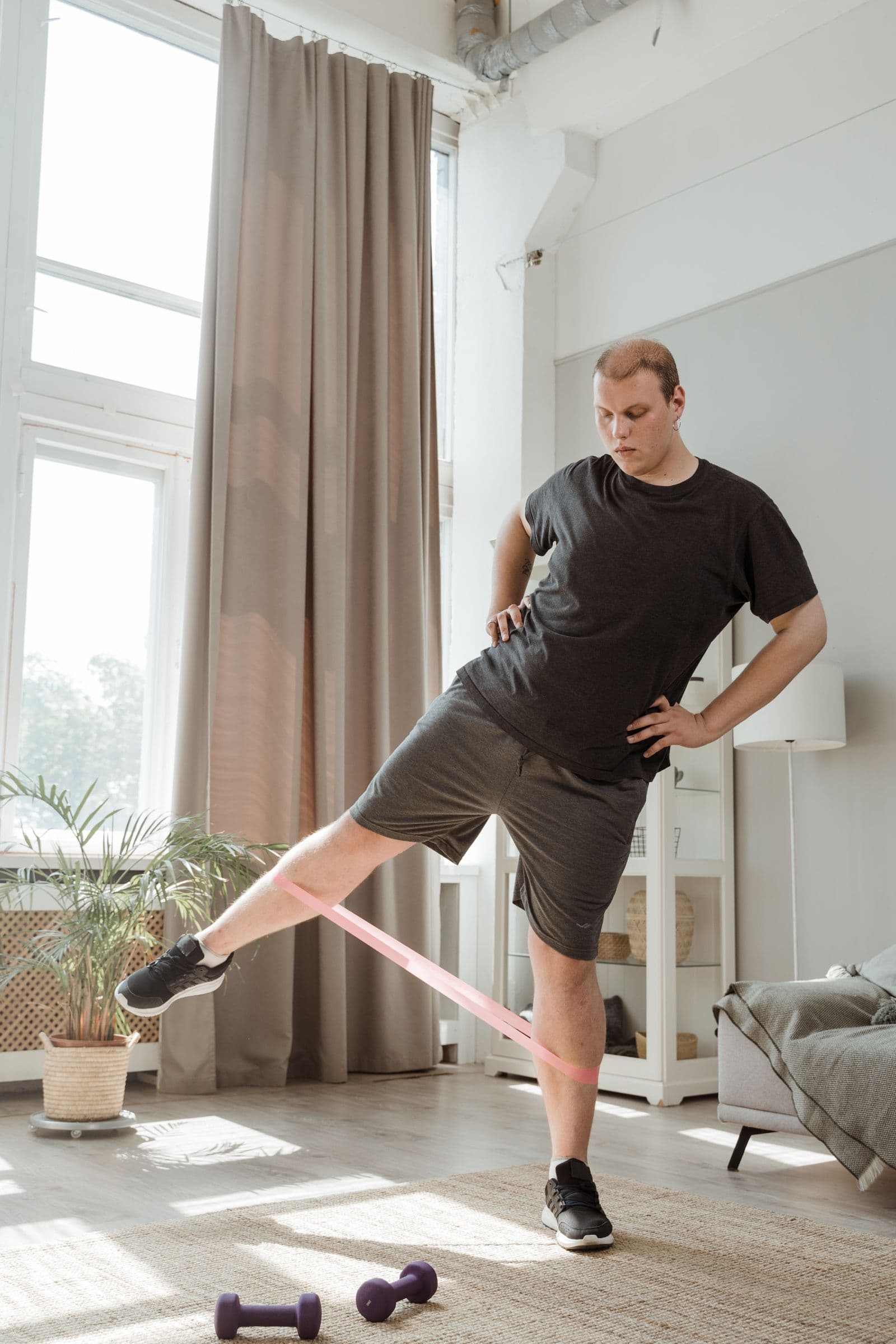 Person performing a controlled resistance band hip exercise at home with dumbbells on the floor nearby