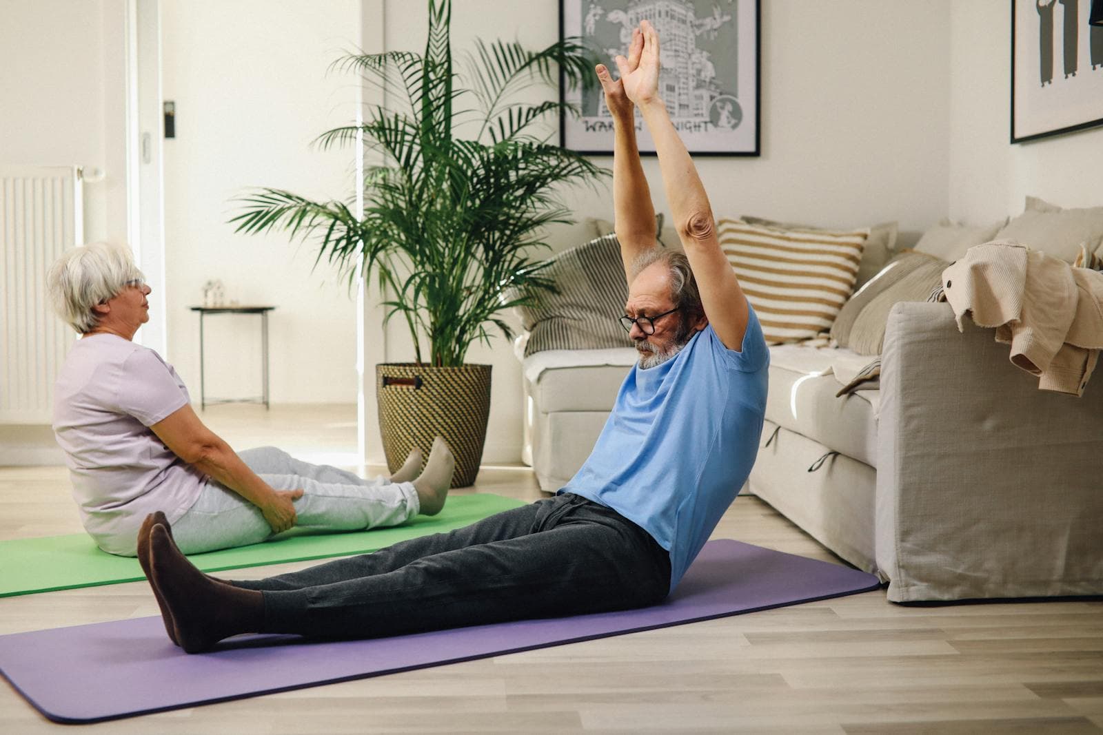 Older couple sitting on yoga mats doing light stretching at home