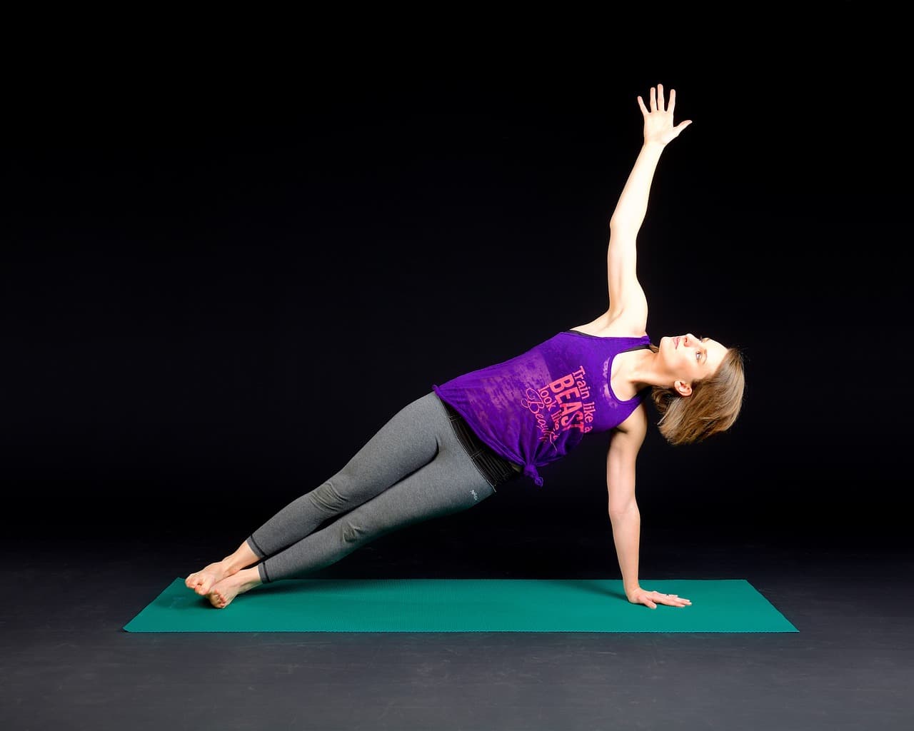 Woman holding a side plank with arm extended overhead, demonstrating lateral chain core stability