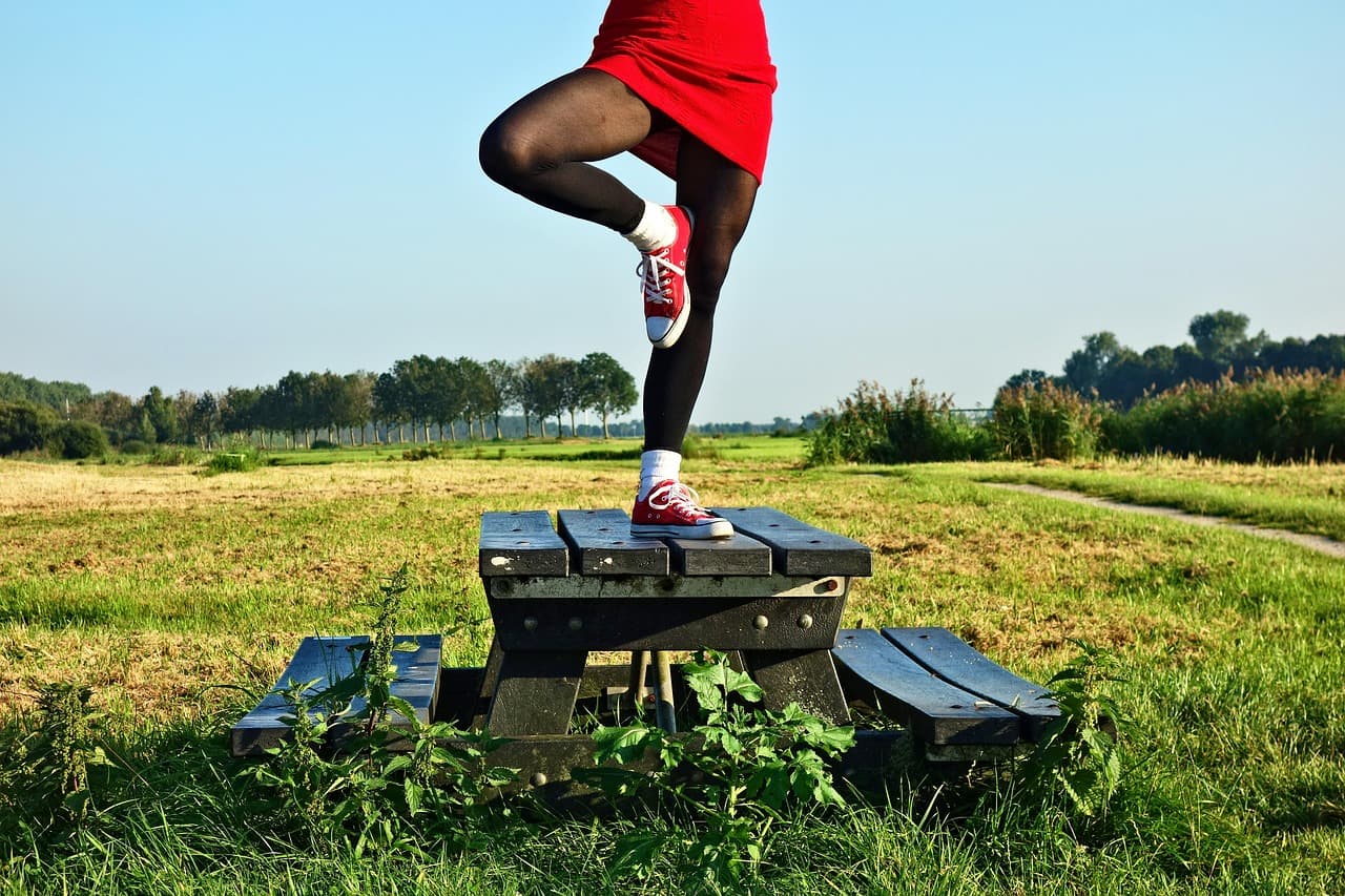 Person balancing on one leg outdoors with the opposite foot tucked against the standing leg, arms out for stability