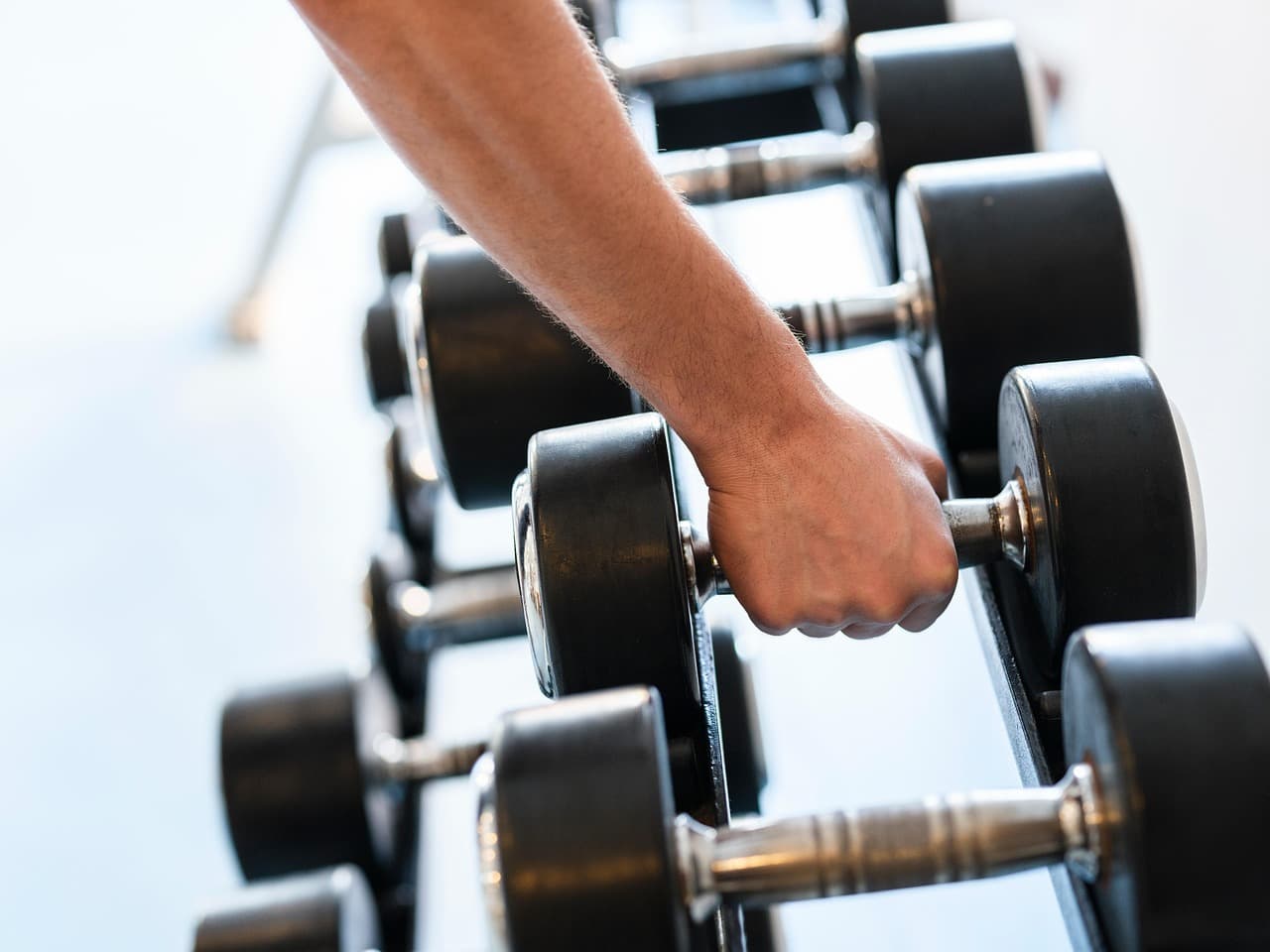Hand reaching to grip a dumbbell on a gym rack