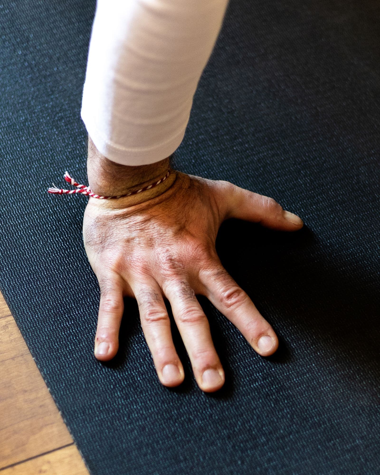 Close-up of a hand pressed flat on a dark yoga mat, fingers spread, wrist bent back under load, sleeve pulled up the forearm
