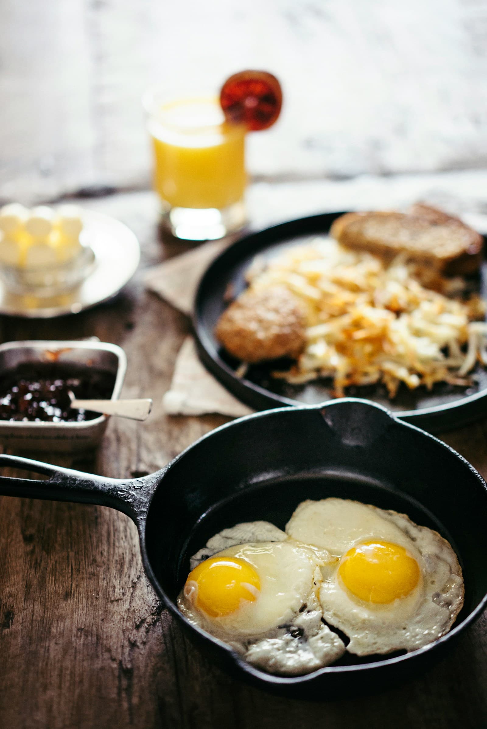 Cast iron skillet with two fried eggs next to a plate of hash browns and toast