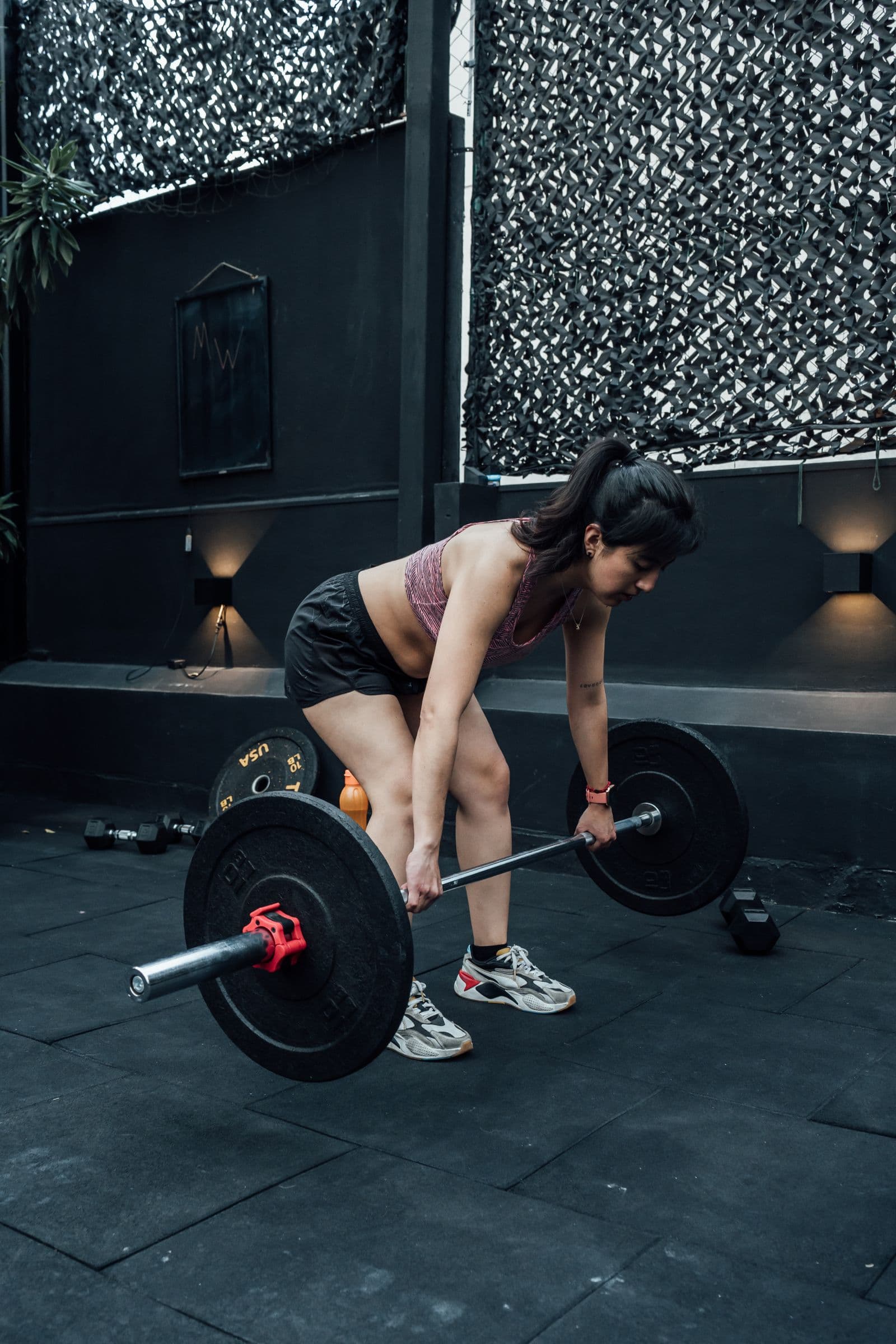 A woman at the bottom of a barbell deadlift with her hips back, spine long and the bar close to her shins
